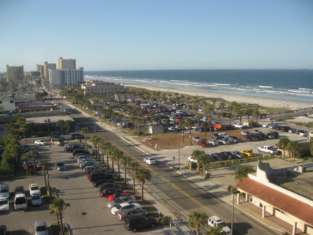 Fahrzeuge sind in der Nähe von Bäumen, Gebäuden und einem Ozean geparkt.