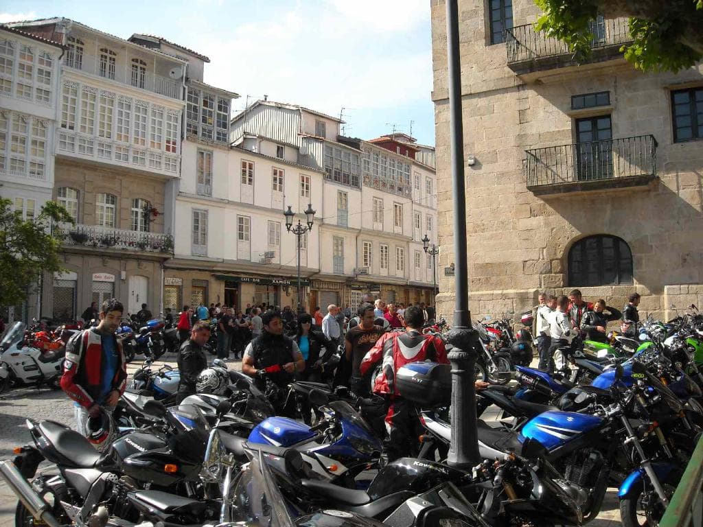 Ein cremefarbenes Gebäude mit zahlreichen Fenstern, angrenzend an ein Backsteingebäude mit einer Metallbalustrade, mit mehreren abgestellten Fahrrädern und Menschen, die sich vor dem Gebäude unterhalten.