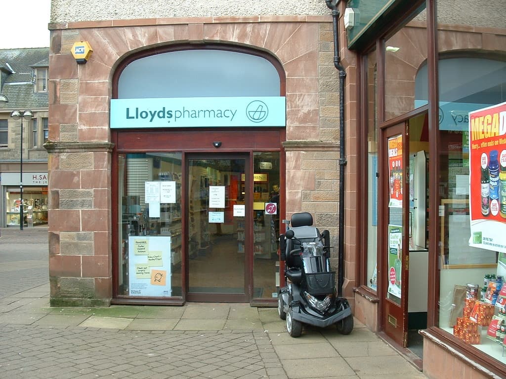 Eine Apotheke mit einem Fahrzeug davor und einem Gebäude links im Eck.