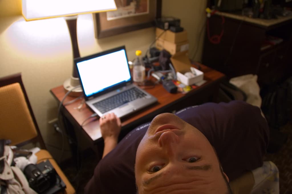 Eine Person, die in einem Stuhl sitzt und auf einem Laptop arbeitet, mit einer Lampe davor, die ihren Kopf nach oben neigt.