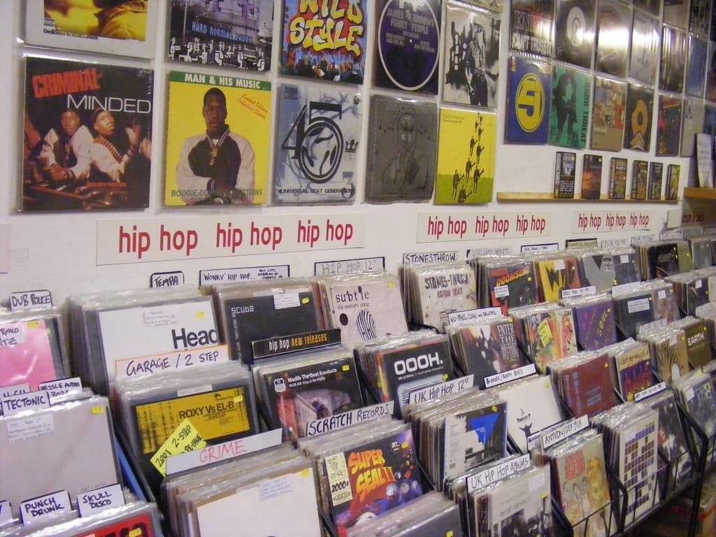 Ein Metallständer mit Büchern und optischen Disc-Hüllen, jede mit Postern versehen, die Text und Bilder zeigen, sowie zusätzlichem Text auf Papieren, die an der Wand in der Mitte befestigt sind.