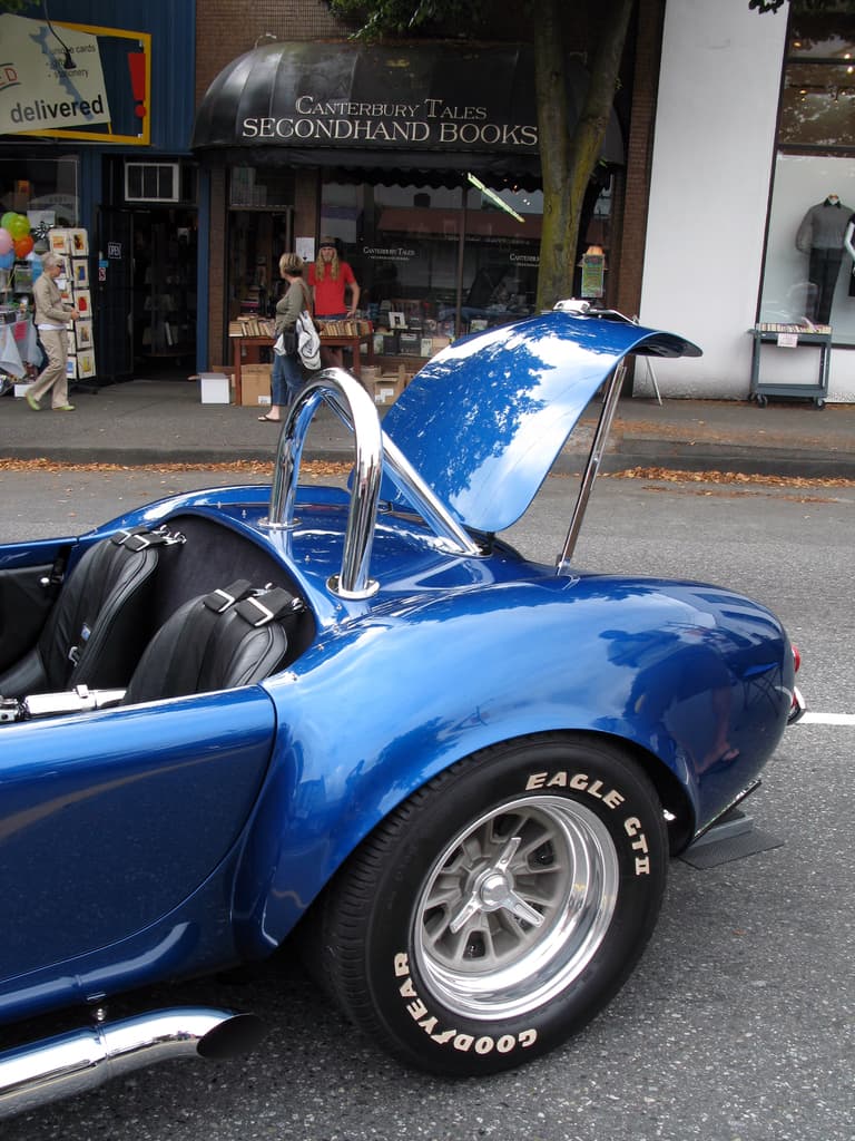 Ein blaues Fahrzeug auf einer Straße mit Geschäften und Menschen im Hintergrund.