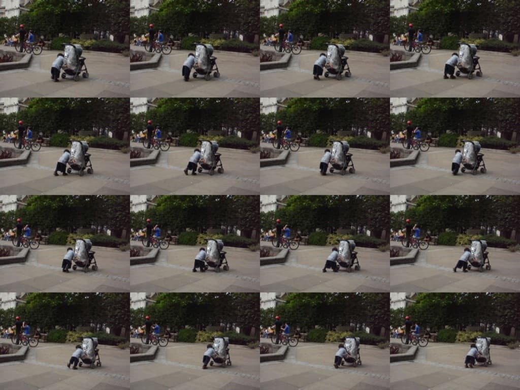 Ein Kind geht auf einer Straße und zieht einen Karren, mit zwei Personen, die links Fahrräder halten, Bäumen im Hintergrund und einem Gebäude links.