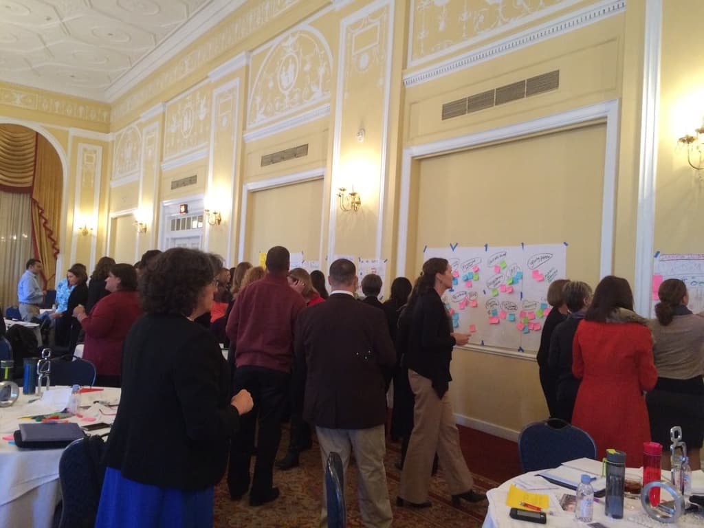 Eine Gruppe von Menschen beobachtet Plakate und Diagramme, die an einer Wand in einem Kunstmuseum zu sein scheinen.