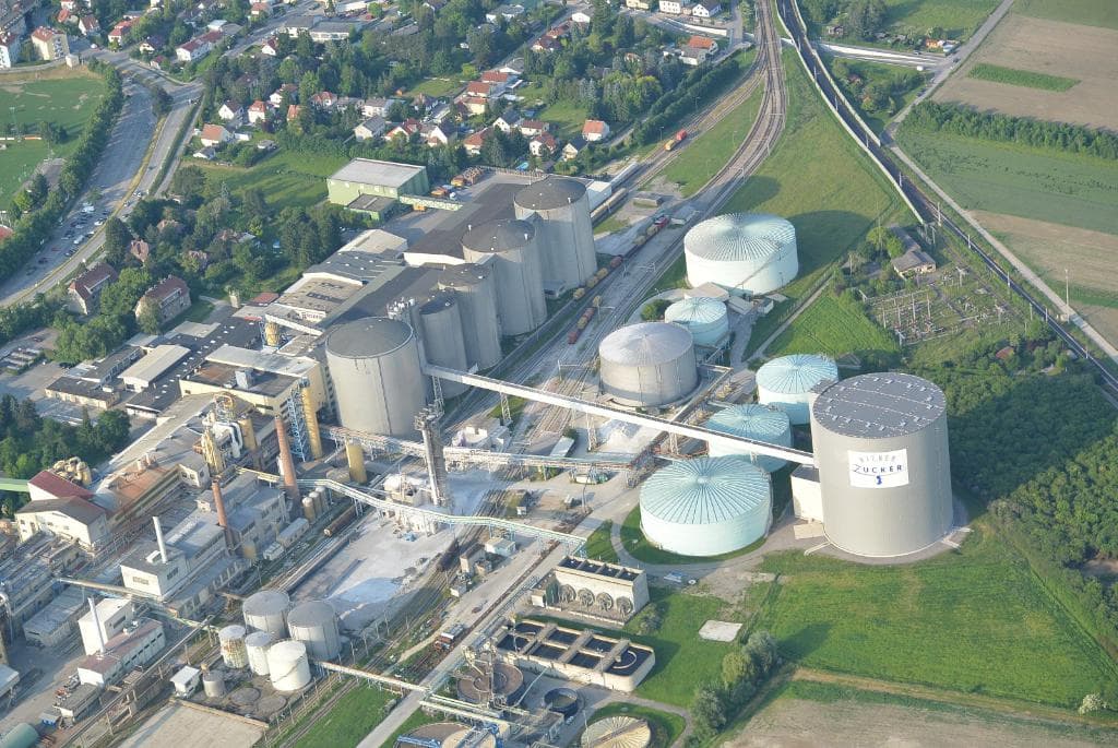 Luftaufnahme eines Vororts mit zahlreichen Gebäuden, Häusern, Bäumen und Fahrzeugen auf den Straßen.