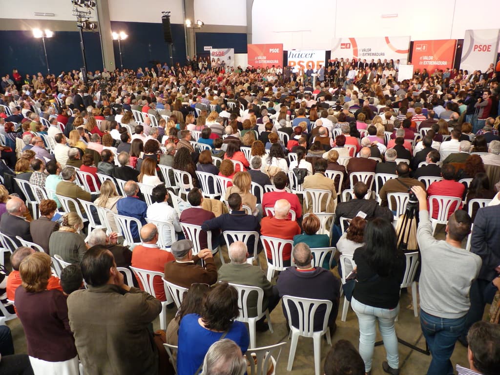Ein volles Stadion mit vielen Sitz- und Stehplätzen, eine Bühne mit zwei Rednern am Podium und zahlreichen Bannern und Lichtern.