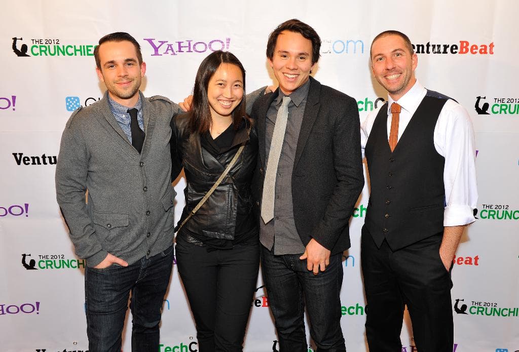 Eine Gruppe strahlender Menschen posiert vor der Kamera mit einem Sponsorenbanner im Hintergrund.