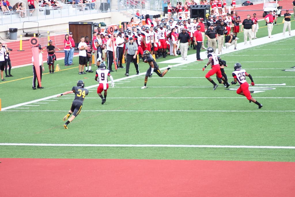 Menschen in schwarzen und weißen Uniformen bei einem Sport auf einem Feld, mit Zuschauern und Kameraleuten im Hintergrund.