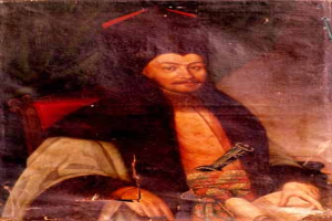 Ein Mann in einem langen Gewand sitzt in einem Stuhl, hält ein Buch und einen Stift in der Hand und hat einen ernsten und nachdenklichen Gesichtsausdruck, während er in die Ferne schaut.