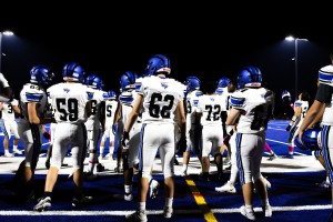 Eine Gruppe von Fußballspielern in Helmen und Fußballschuhen steht auf einem Feld, mit Leuchten im Hintergrund.