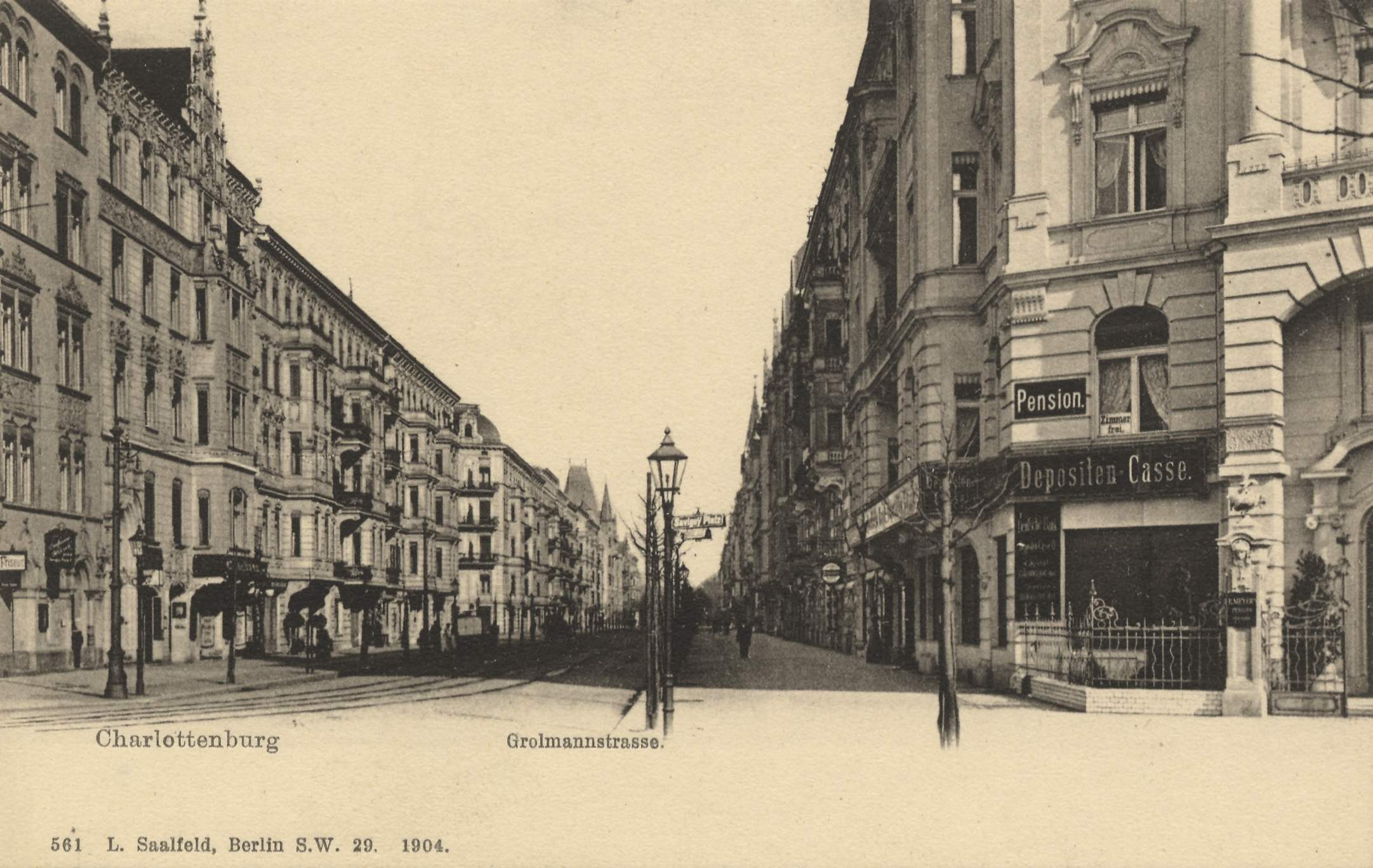 Schwarz-weiß-Foto einer Stadtstraße in Charlottenburg, Deutschland, mit Gebäuden, Straßenlaternen, Schildern, Kraftfahrzeugen, Fußgängern und Gittern unter einem klaren Himmel.