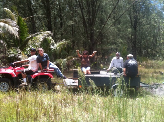 Eine Gruppe von Menschen auf einem Traktor mit einer Person, die es f√§hrt, mit B√§umen im Hintergrund.