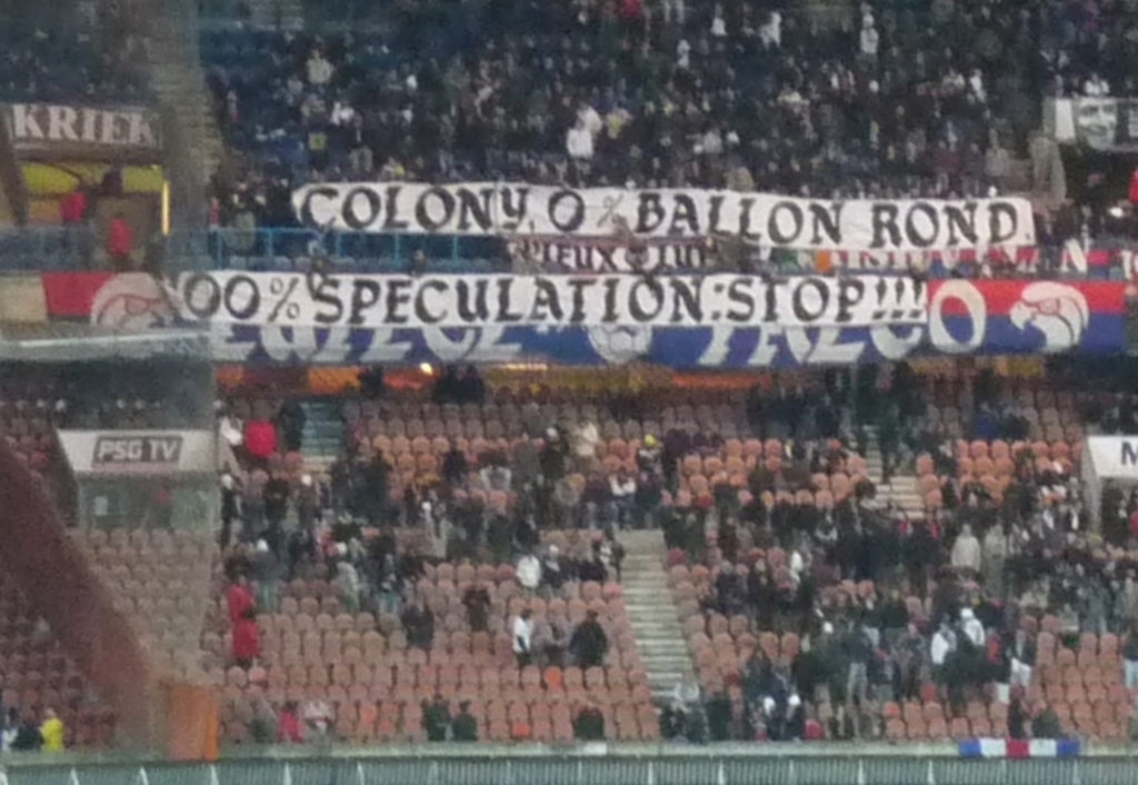 Ein volles Stadion mit Bannern und Stühlen im Vordergrund, einem Zaun unten und einer Treppe auf der linken Seite.