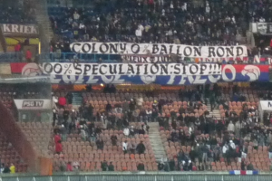 Ein volles Stadion mit Bannern und Stühlen im Vordergrund, einem Zaun unten und einer Treppe auf der linken Seite.