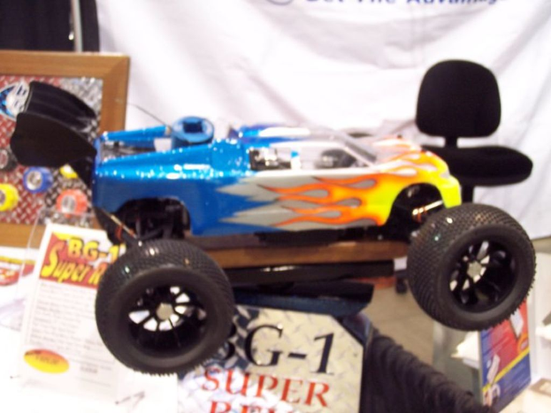 Ein Spielzeugfahrzeug in Blau, Gelb, Weiß und Orange, umgeben von Prospekten, einem Rahmen und einer weißen Fahne.