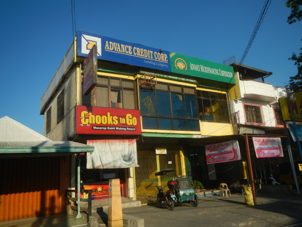 Ein Gebäude mit einer Tafel, auf der "Advance Credit Corp" steht, umgeben von Fahrzeugen, Werbetafeln, Strommasten, Kabeln, Bäumen und einem klaren blauen Himmel.
