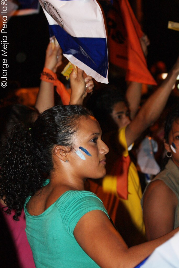 Frauen in grünen T-Shirts bei einer Demonstration, die weiße Stoffbahnen halten, mit anderen Mädchen im Hintergrund.