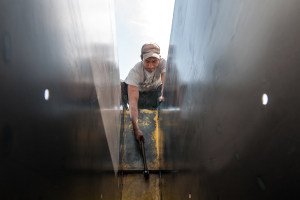 Ein Mann in T-Shirt, Hose und Mütze schlägt mit einem Hammer auf ein Objekt ein.
