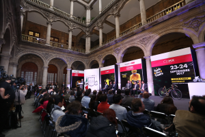 Eine Gruppe von Menschen, die an einem Tisch mit einem Podium und einem Mikrofon vor einer Menge, Kameras und Schildern sitzen, während einer Pressekonferenz für das CDMX 2017-Event.