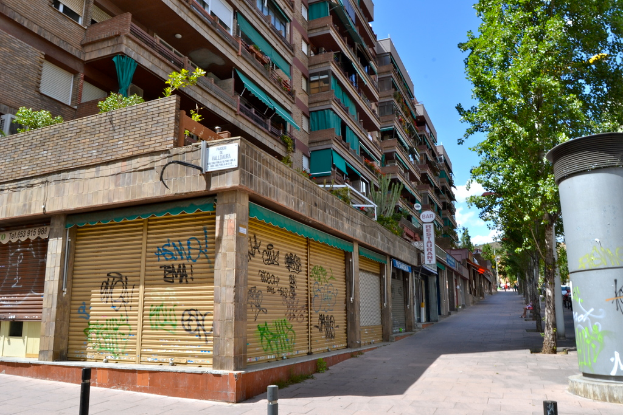 Eine Szene mit Gebäuden mit Fenstern, grüner Kleidung, Geschäften, Schildern und umliegenden Bäumen und Pflanzen.