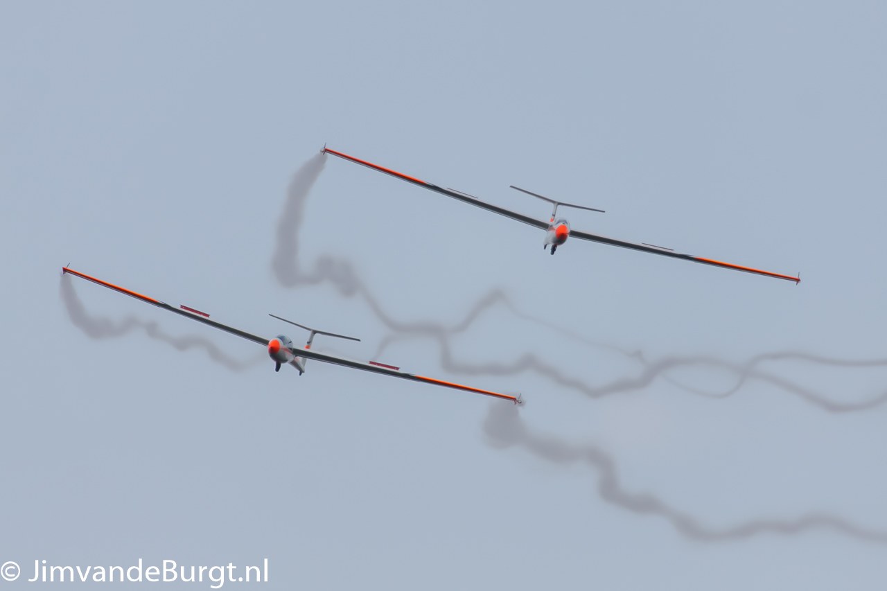 Zwei Segelflugzeuge am Himmel mit Rauchspuren, mit Text in der linken unteren Ecke.