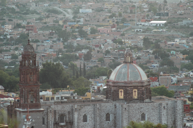 Eine Luftaufnahme einer Stadt mit Bäumen, Gebäuden, Straßen und Masten, die eine Kirche im Vordergrund zeigt.