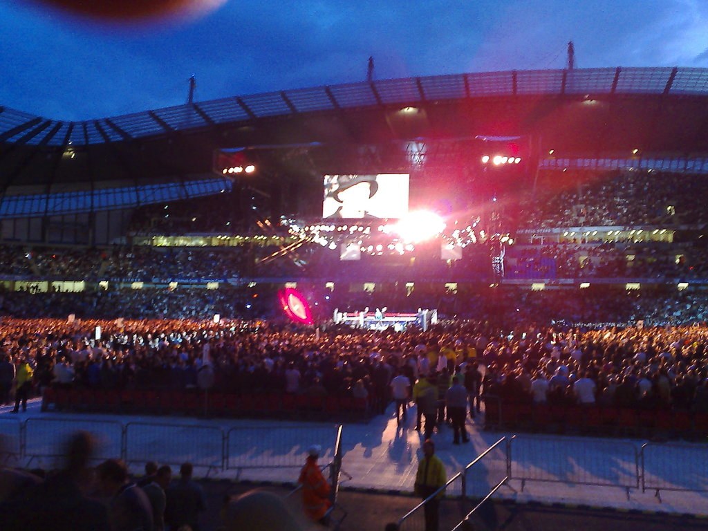 Konzertort mit Menschen, Bühnenbeleuchtung und einem Projektionsschirm.