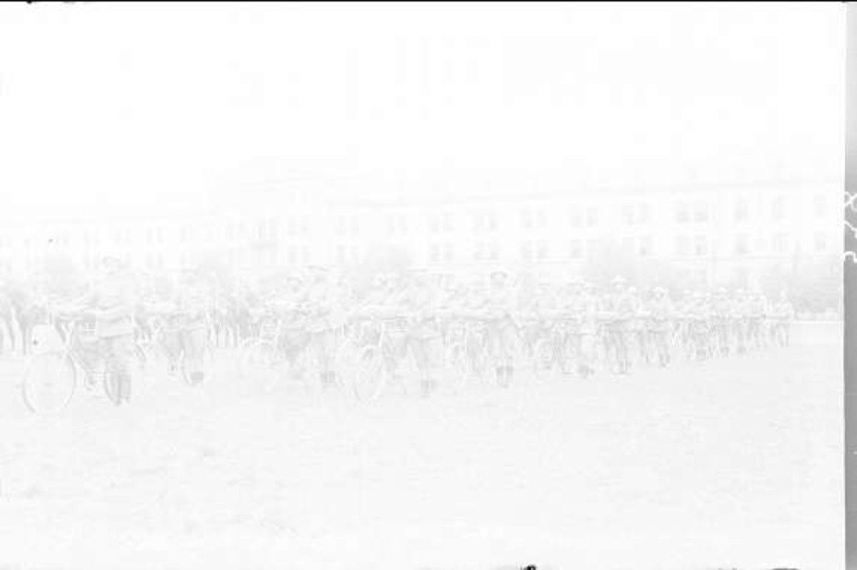 Schwarzes und weißes Foto von Radrennfahrern im Schnee an einem Gebäude im Hintergrund.