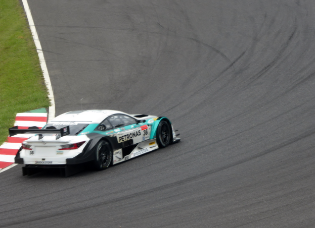 Ein Mercedes-AMG GT3 Rennauto fährt auf einer Rennstrecke mit Text auf dem Auto und Gras auf der linken Seite der Strecke.