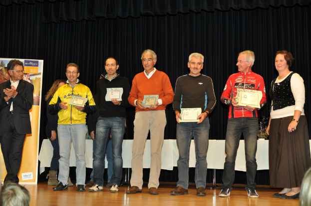 Eine Gruppe von Menschen auf einer Bühne mit Zertifikaten in der Hand, im Hintergrund ein Banner, ein Tisch daneben und ein schwarzer Vorhang.
