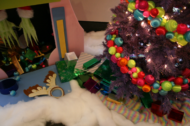 Drinnen steht rechts ein geschmÃ¼ckter Weihnachtsbaum mit Lichterkette und Schmuck, in der Mitte Geschenkboxen und Deko, links oben eine HÃ¼tte mit Deko und unten Wolle und WÃ¤sche.