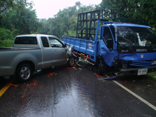Ein schwer beschädigtter Lkw mit eingedellter Front und verbeulter Karosserie liegt auf der Seite einer Straße, umgeben von Bäumen unter einem klaren blauen Himmel.