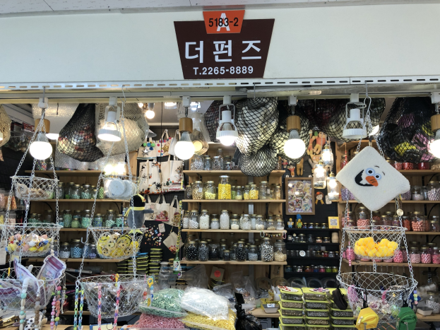 Ein unordentlicher Laden in Seoul, der verschiedene Gegenstände wie Körbe, Lichter, Flaschen und Spielzeuge auf Regalen ausstellt, mit einem Schild öber dem Eingang, das ihn als einen der besten koreanischen Läden ausweist.