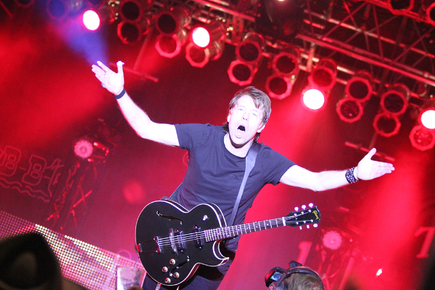 Eine Person, die eine Gitarre spielt und in einem dunklen Hintergrund singt.