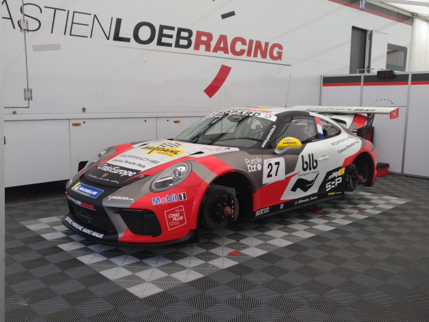 Ein Porsche 911 GT3 RSR in einer Garage mit einer Wandbeschriftung und einer Tür im Hintergrund geparkt.