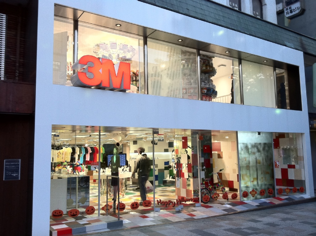 Ein Gebäude mit einer Glaswand, auf der Kleider an Bügeln hängen, eine Schaufensterpuppe, ein Fahrrad, aufgeklebte Bilder und Schrift auf der Glaswand.