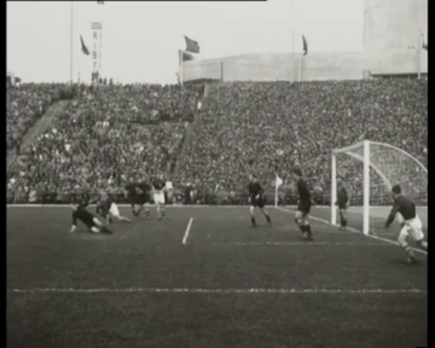 Ein Schwarz-Weiß-Foto eines Fußballspiels in einem Stadion, mit Spielern auf dem Feld und einem Torpfosten auf der rechten Seite, Zuschauern in den Rängen und Fahnen mit Stangen im Hintergrund. Der Text "1958-1958 WM-Finale - Manchester United v Liverpool" wird oben und unten im Bild angezeigt.