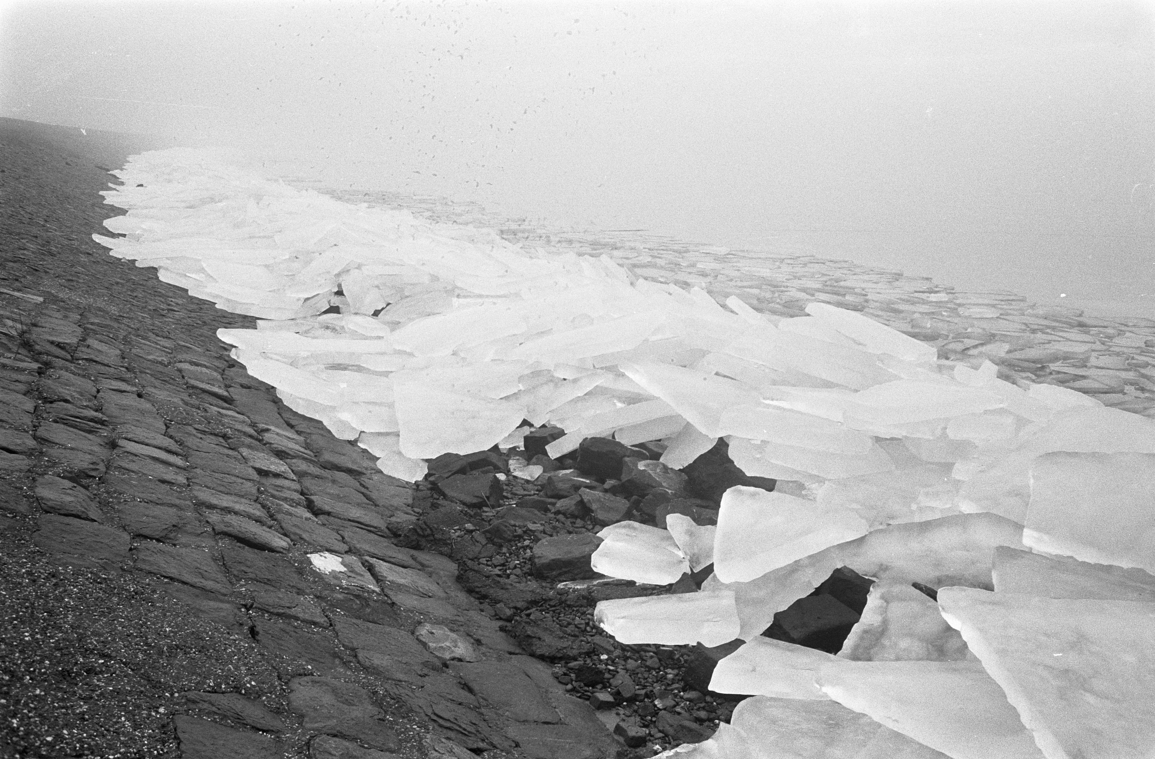 Ein Schwarz-Weiß-Foto eines großen, gebrochenen Eisstücks auf dem Boden mit verstreuten Eissplittern und dem Himmel im Hintergrund.