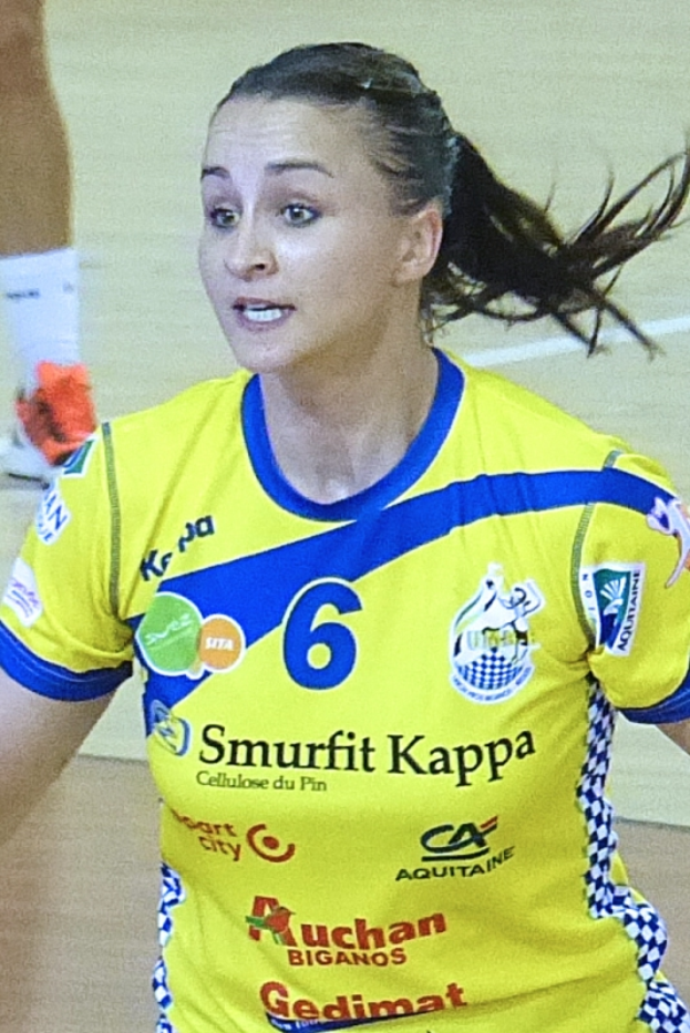 Eine Frau in einer gelben und blauen Uniform, die Volleyball spielt, mit einem menschlichen Bein im Hintergrund.