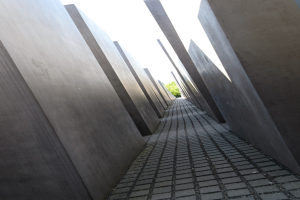Luftaufnahme des Holocaust-Mahnmals für die ermordeten Juden Europas in Berlin mit Reihen von Betonsteinen und Bäumen sowie einem klaren Himmel im Hintergrund.