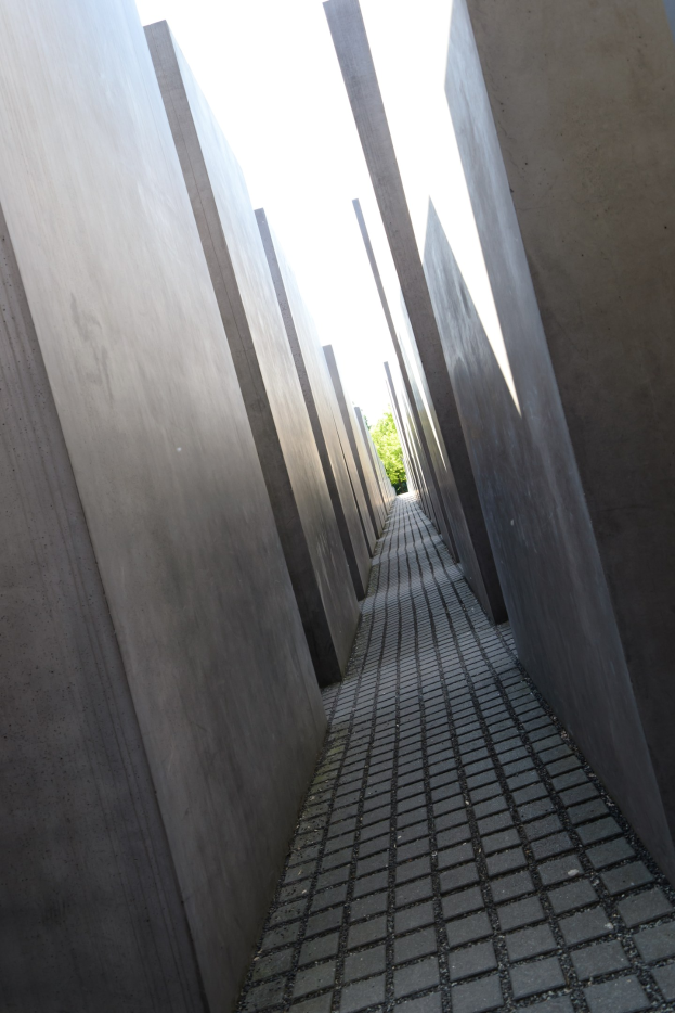 Luftaufnahme des Holocaust-Mahnmals für die ermordeten Juden Europas in Berlin mit Reihen von Betonsteinen und Bäumen sowie einem klaren Himmel im Hintergrund.