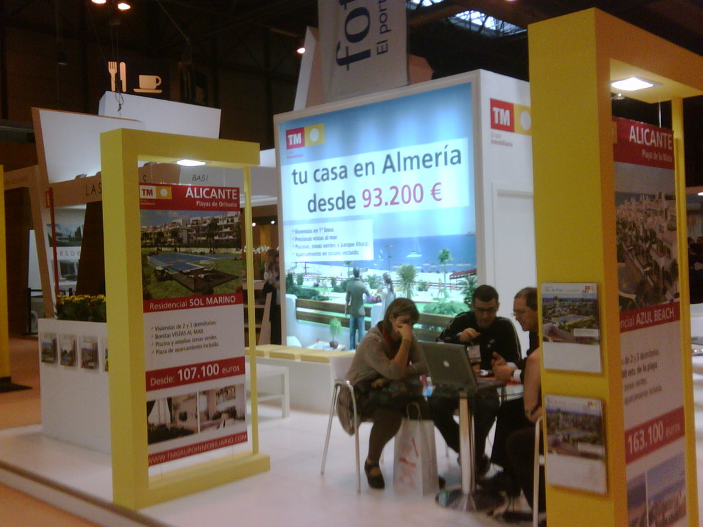 Ein Raum mit Menschen an einem Tisch, die auf Laptops arbeiten, mit mehreren Flyern mit verschiedenen Werbeanzeigen daneben.