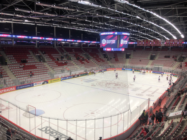 Ein Eishockeyspiel in einer großen Arena mit Sitz- und Stehplätzen, einem Zaun um die Eisfläche, einem Display mit der Aufschrift "St. Louis Blues vs Detroit Red Wings", Metallrahmen und einer Decke mit Deckenleuchten.