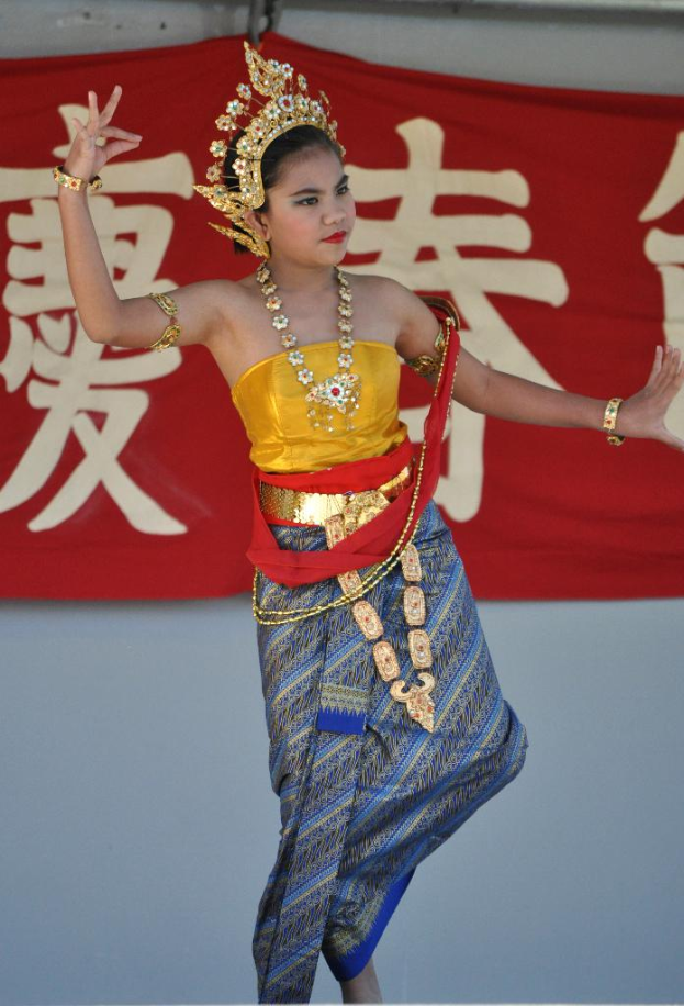 Ein Mädchen tanzt in traditioneller Kleidung und Schmuck mit einem Banner mit Text dahinter.