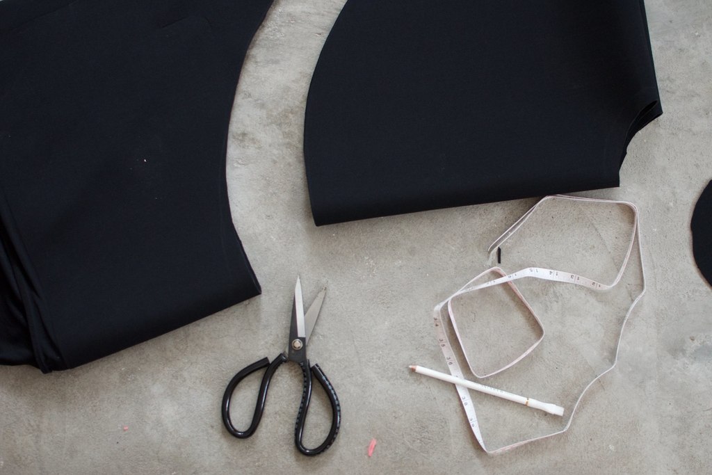 Schere, Bleistift, Maßband und Kleidung liegen auf dem Boden verstreut.