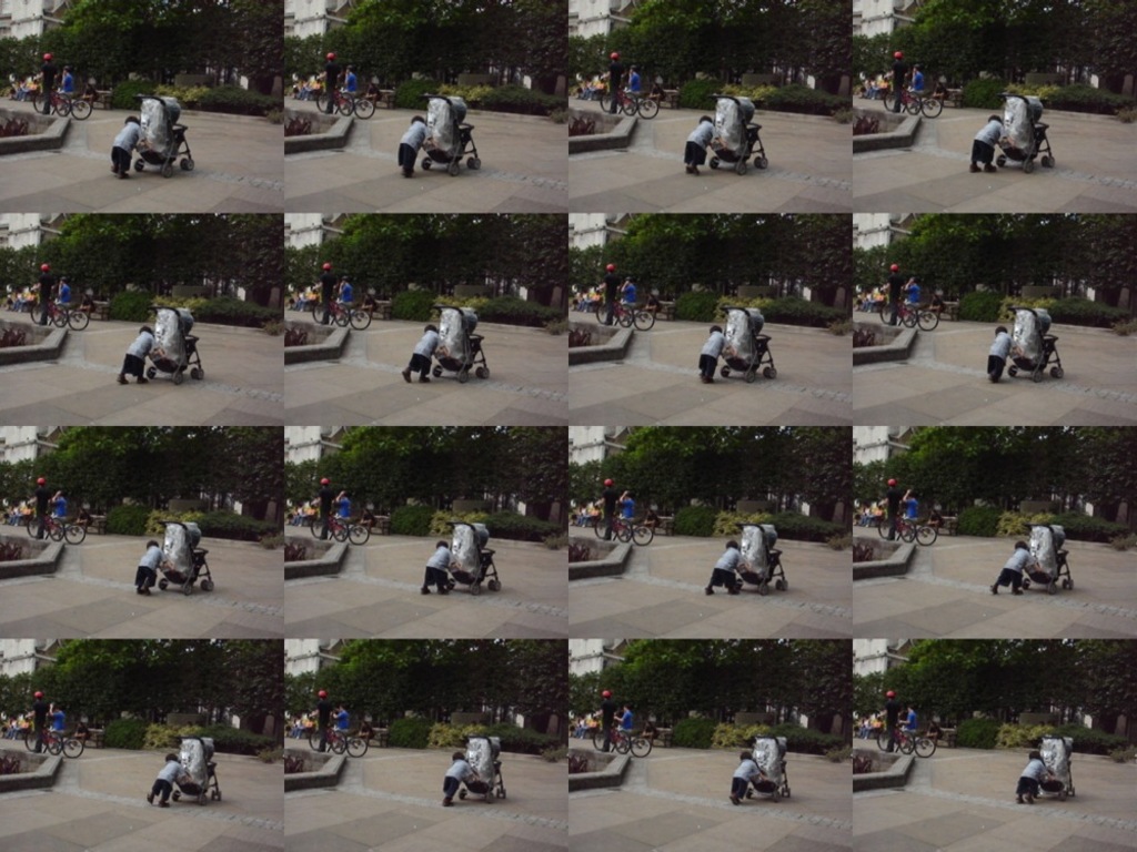 Ein Kind geht auf einer Straße und zieht einen Wagen, mit zwei Personen auf der linken Seite, die Fahrräder halten, und einem Gebäude und Bäumen im Hintergrund.