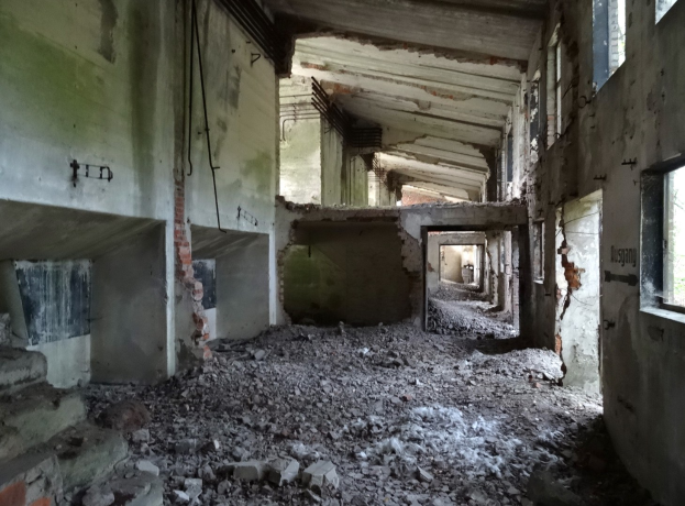 Altes Gebäude mit erheblichen strukturellen Schäden, zerbrochene Fenster, verstreute Trümmer, freiliegende Rohre und Schutt.