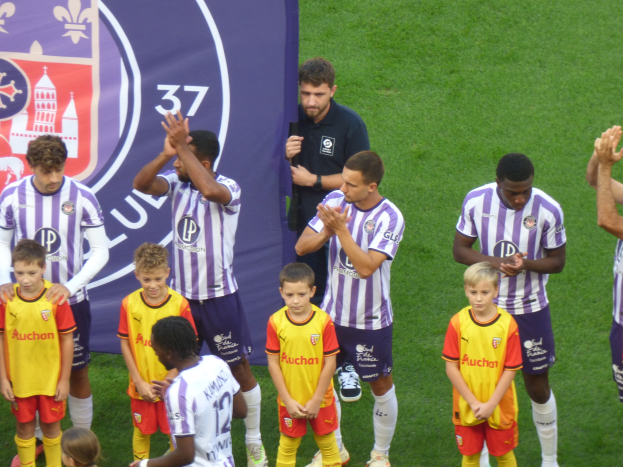 Junge Jungs auf einem Fußballfeld, die klatschen, mit einem Banner und Logos im Hintergrund.