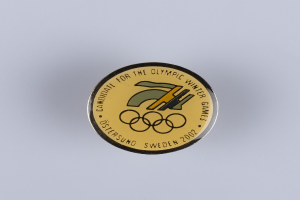 Ein runder Abzeichenaufnäher mit schwarzem Hintergrund und goldfarbenem Olympia-Winterspielen-Logo in der Mitte, mit der Beschriftung "Olympische Winterspiele" in fetter weißer Schrift.