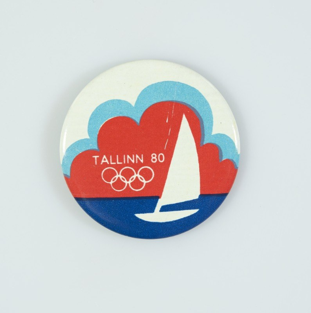 Ein weißer Anstecker mit einem Segelboot-Design und der Aufschrift "Tallinn 80 Olympische Spiele", der das 80-jährige Jubiläum der Olympischen Spiele in Tallinn feiert.
